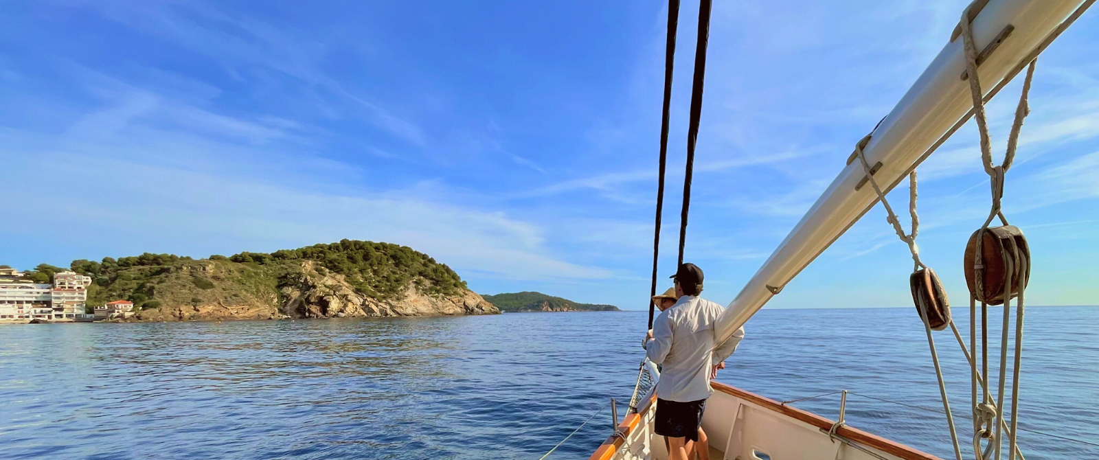 A man and woman on a sailboat looking out to the coast.