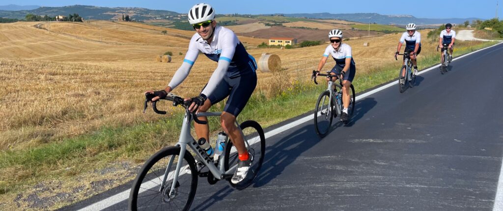 A group of cyclists riding alongside wheat fields of Tuscany