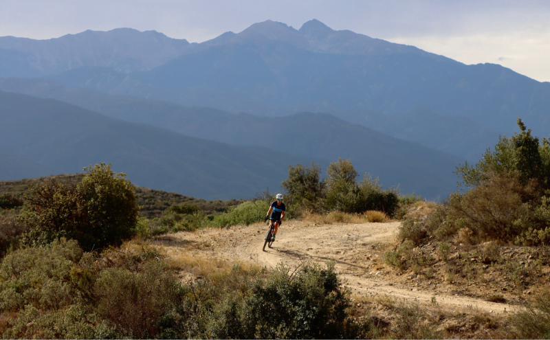 Single cyclist on gravel road with mountains in the background